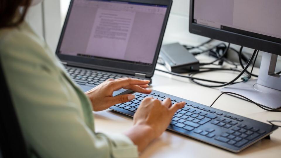 Una mujer escribe un texto en la computadora.
