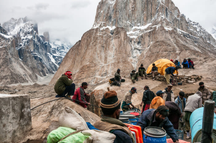 porters sitting on rocks during a break with Cathedral tower behind, Karakoram Pakistan