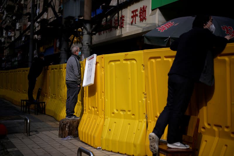 Residents wearing face masks pay for groceries by standing on chairs to peer over barriers set up to ring fence a wet market on a street in Wuhan