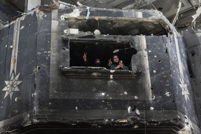 Palestinian women gesture from their window of their destroyed home, as people salvage usable items from the rubble following months of Israeli bombardment, in Khan Yunis, Gaza. Photo by Ismael Mohamad/UPI