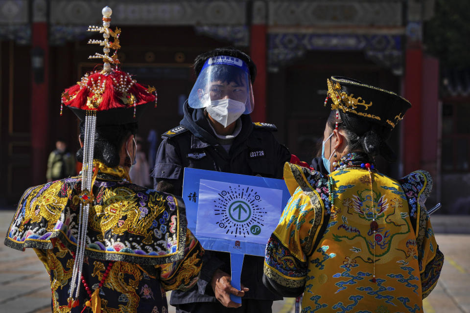 A security guard wearing a face shield and mask asks visitors wearing the emperor and empress costumes to scan their traveling code before entering to the Forbidden City during the opening ceremony of the 20th National Congress of China's ruling Communist Party in Beijing, China on Sunday, Oct. 16, 2022. The overarching theme emerging from China's ongoing Communist Party congress is one of continuity, not change. The weeklong meeting is expected to reappoint Xi Jinping as leader, reaffirm a commitment to his policies for the next five years and possibly elevate his status even further as one of the most powerful leaders in China's modern history. (AP Photo/Andy Wong)