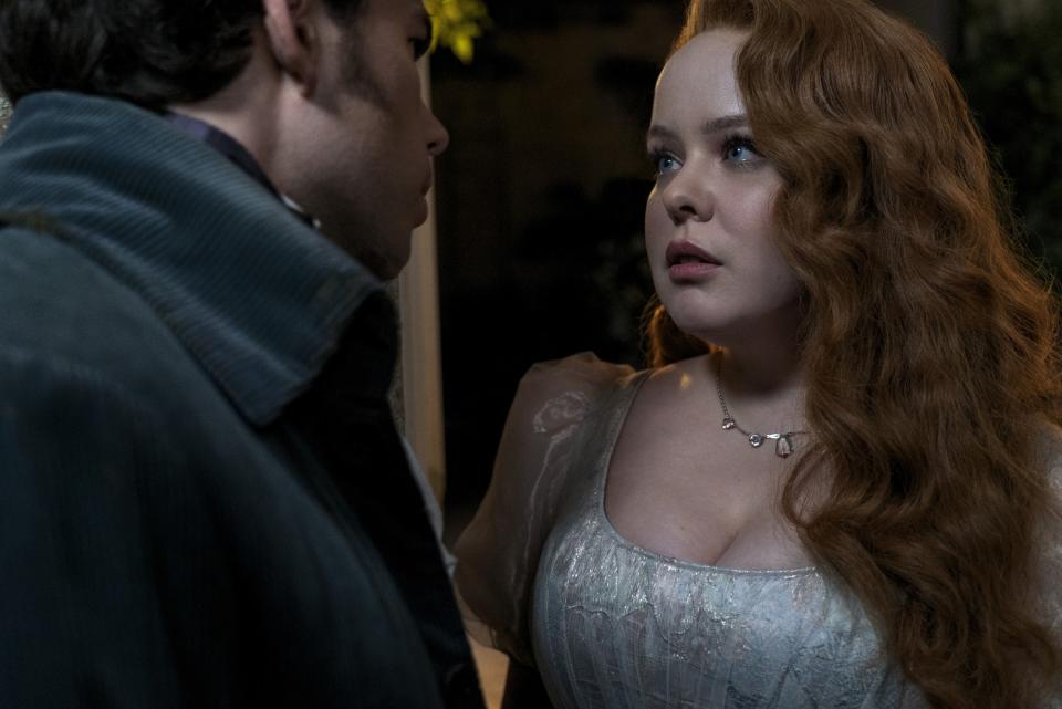 Nicola Coughlan and Luke Newton in a period drama scene. Nicola wears a vintage-style dress with puffed sleeves and a pearl necklace