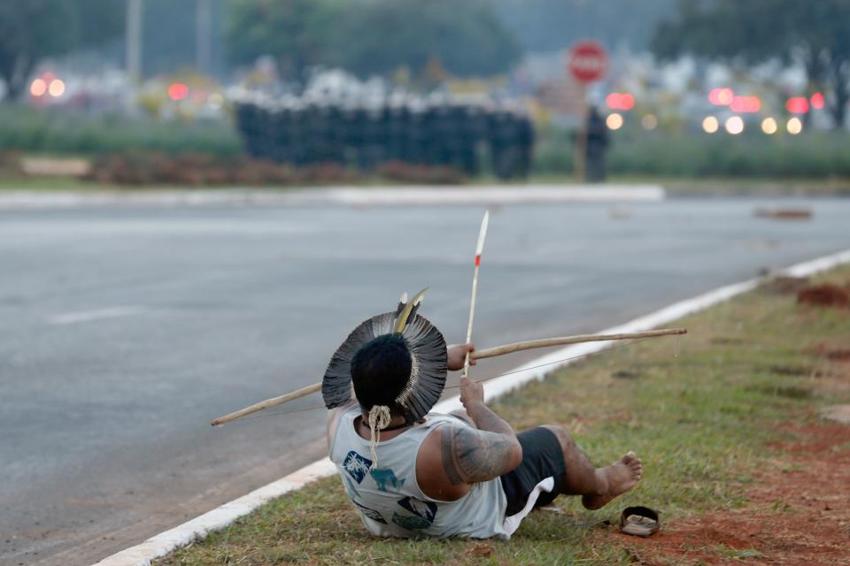 An Indigenous protester in traditional headdress gets ready to fire an arrow against the military police