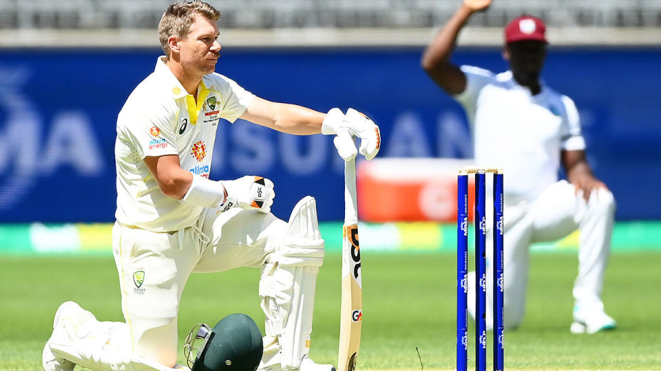 David Warner is pictured taking a knee, with a West Indies playing doing the same in the background.