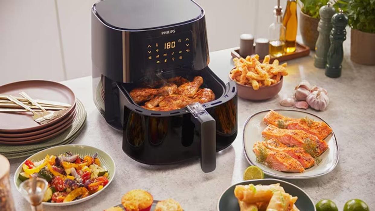  A Philips air fryer with an open draw full of food, surrounded by plates of food. 