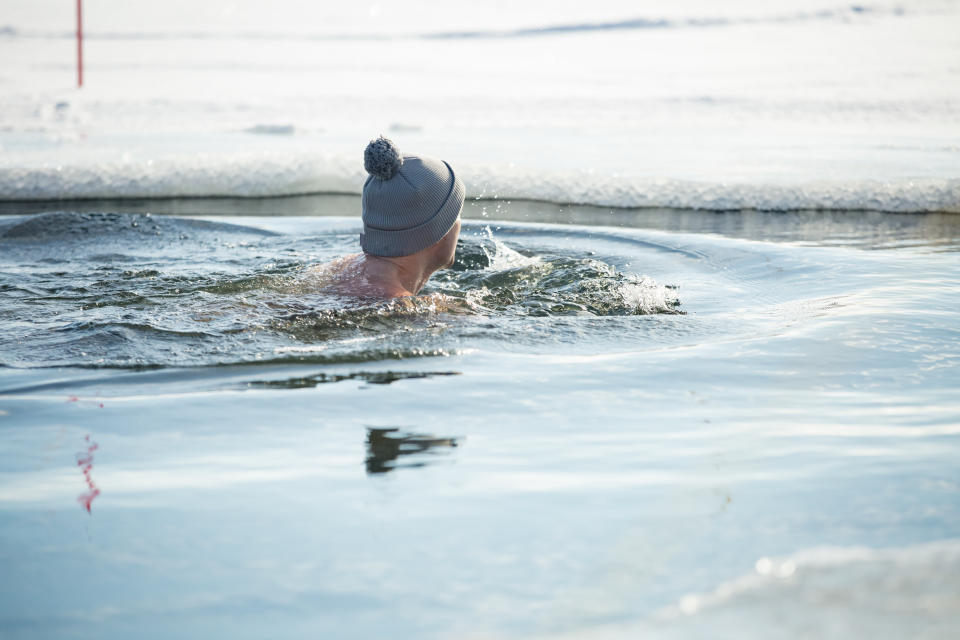 A person wearing a ski hat swims in a body of water surrounded by what looks like snow and ice. 