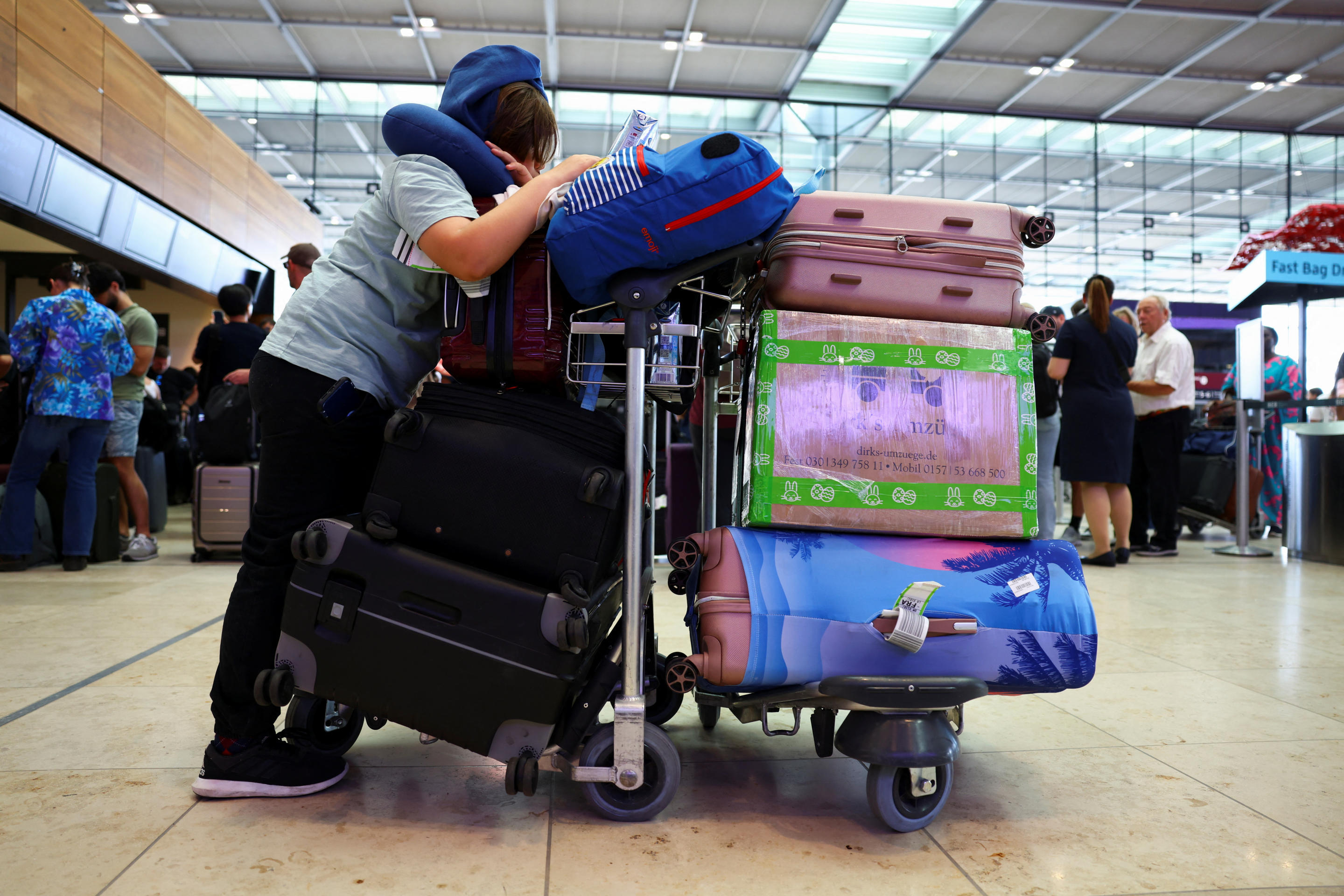 A person with piles of suitcases and bags on a luggage cart at Berlin airport.