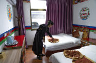 A woman in ethnic dress adjusts a bedspread at her tourist homestay in Zhaxigang village near Nyingchi in western China's Tibet Autonomous Region, Friday, June 4, 2021. Tourism is booming in Tibet as more Chinese travel in-country because of the coronavirus pandemic, posing risks to the region's fragile environment and historic sites. (AP Photo/Mark Schiefelbein)