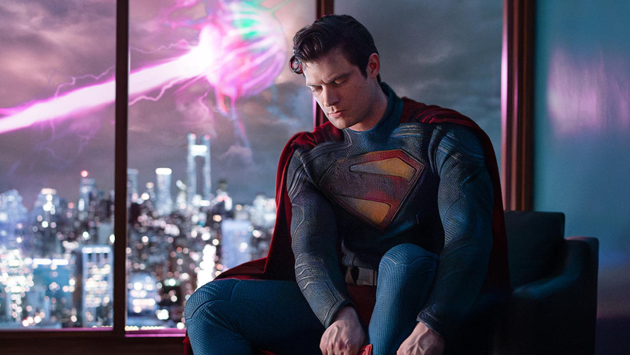  A screenshot of David Corenswet's Man of Steel suiting up in a Metropolis apartment while a pink lazer is fired in the background in 2025's Superman film. 