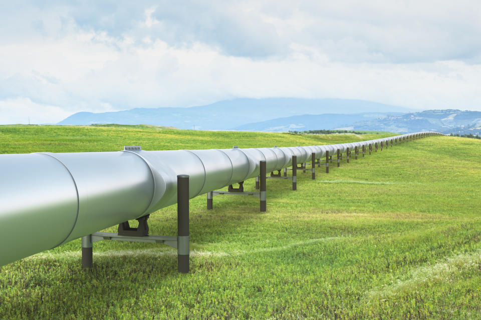 A pipeline in a green field heading off to the mountains.