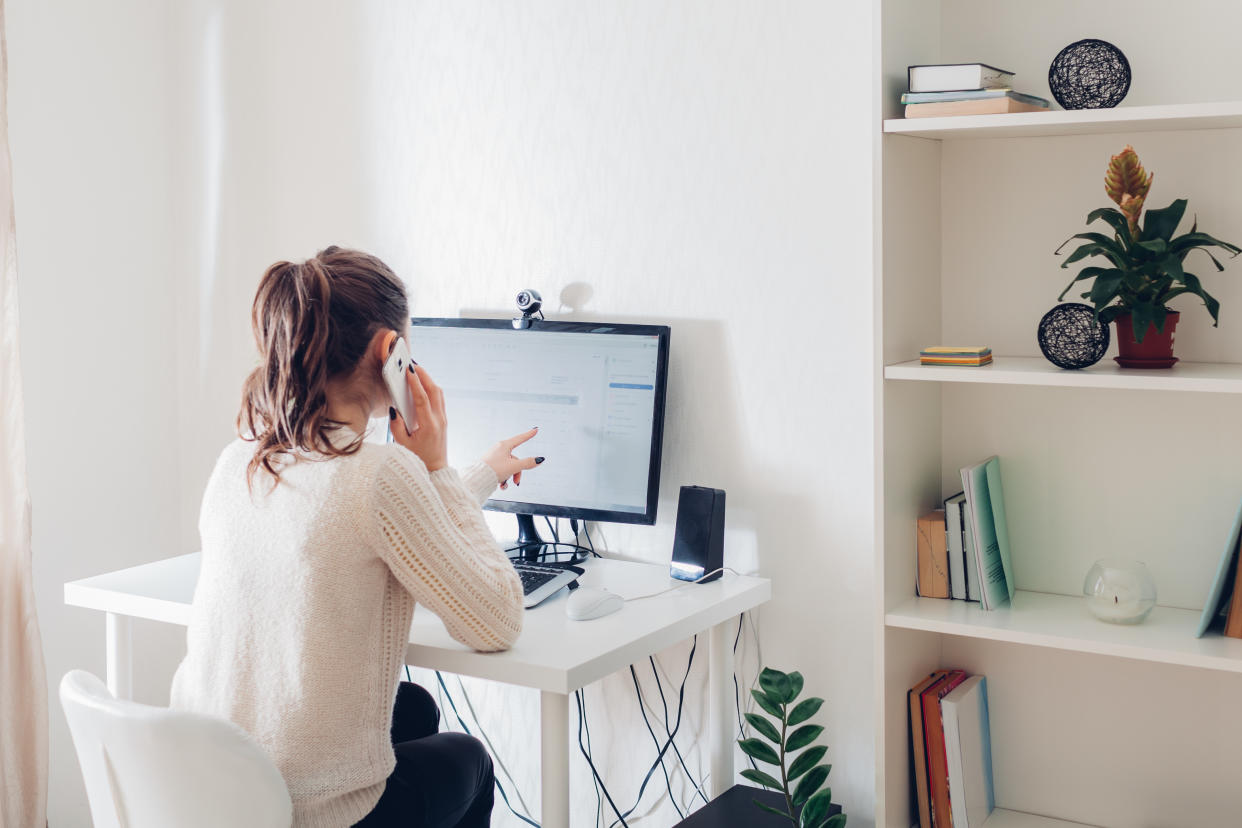 Work from home during coromavirus pandemic. Woman stays home talking on phone. Workspace of freelancer. Office interior with computer