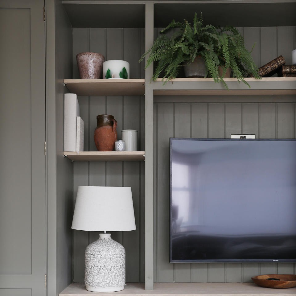  TV mounted on panelled media wall with shelving, decorated with table lamps, vases, and books. 