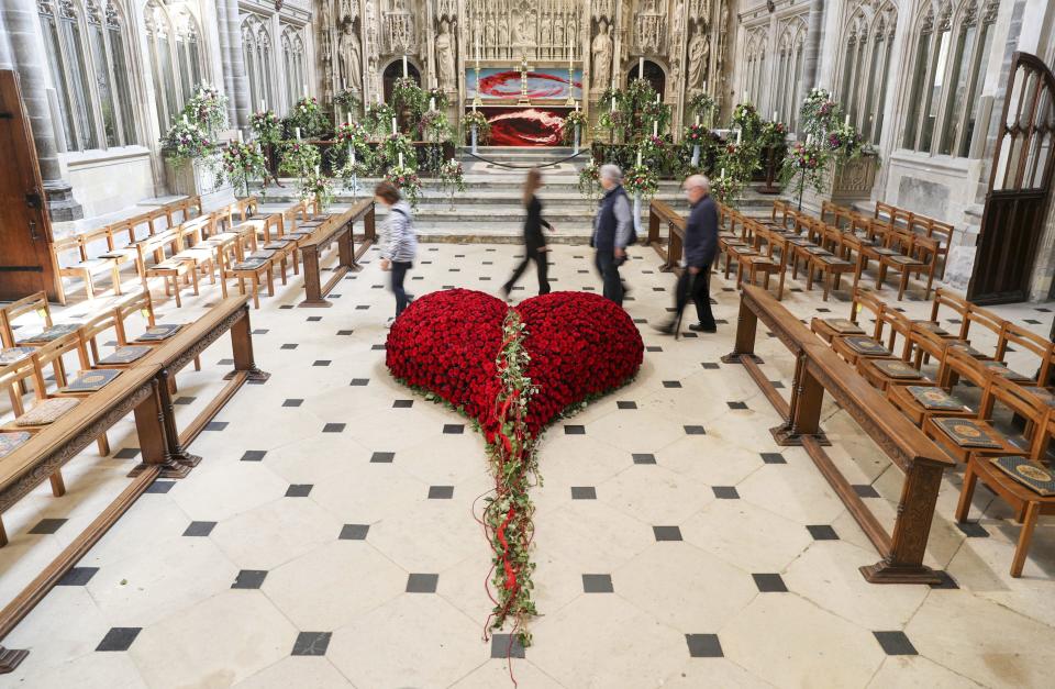 People walk past a heart made out of red roses in Winchester Cathedral in Winchester, England