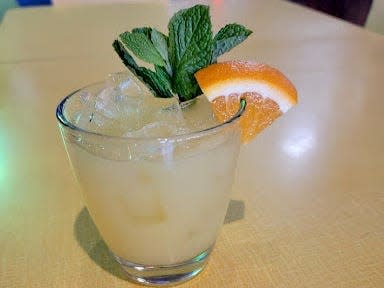 A rum with pineapple juice with mint and orange garnish