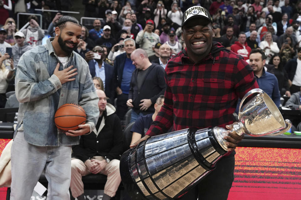 Toronto Argonauts' Henoc Muamba holds the CFL Grey Cup as Drake, left, looks on during a break in the first half of an NBA basketball game between the Brooklyn Nets and the Toronto Raptors on Wednesday, Nov. 23, 2022, in Toronto. (Chris Young/The Canadian Press via AP)
