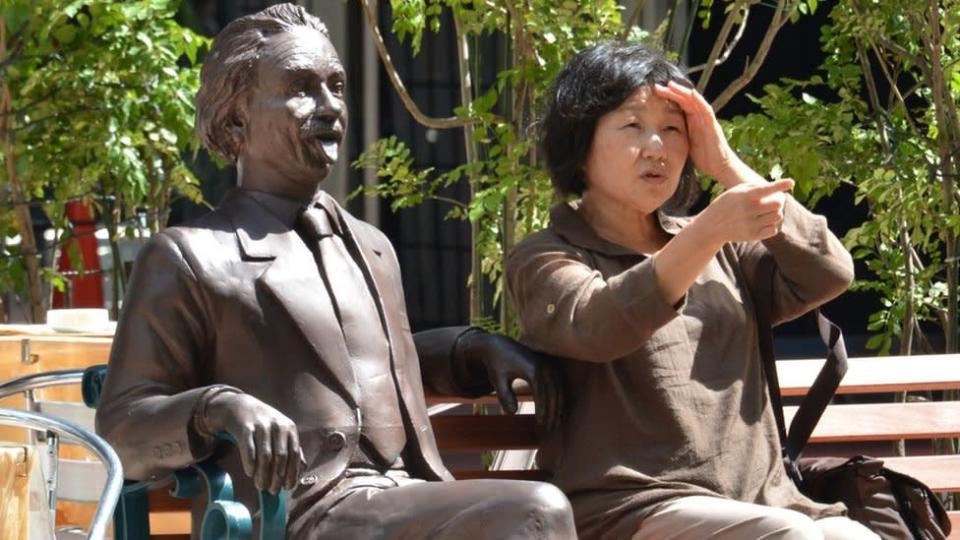 Una se&#xf1;ora sentada en un banco con una estatua de Einstein