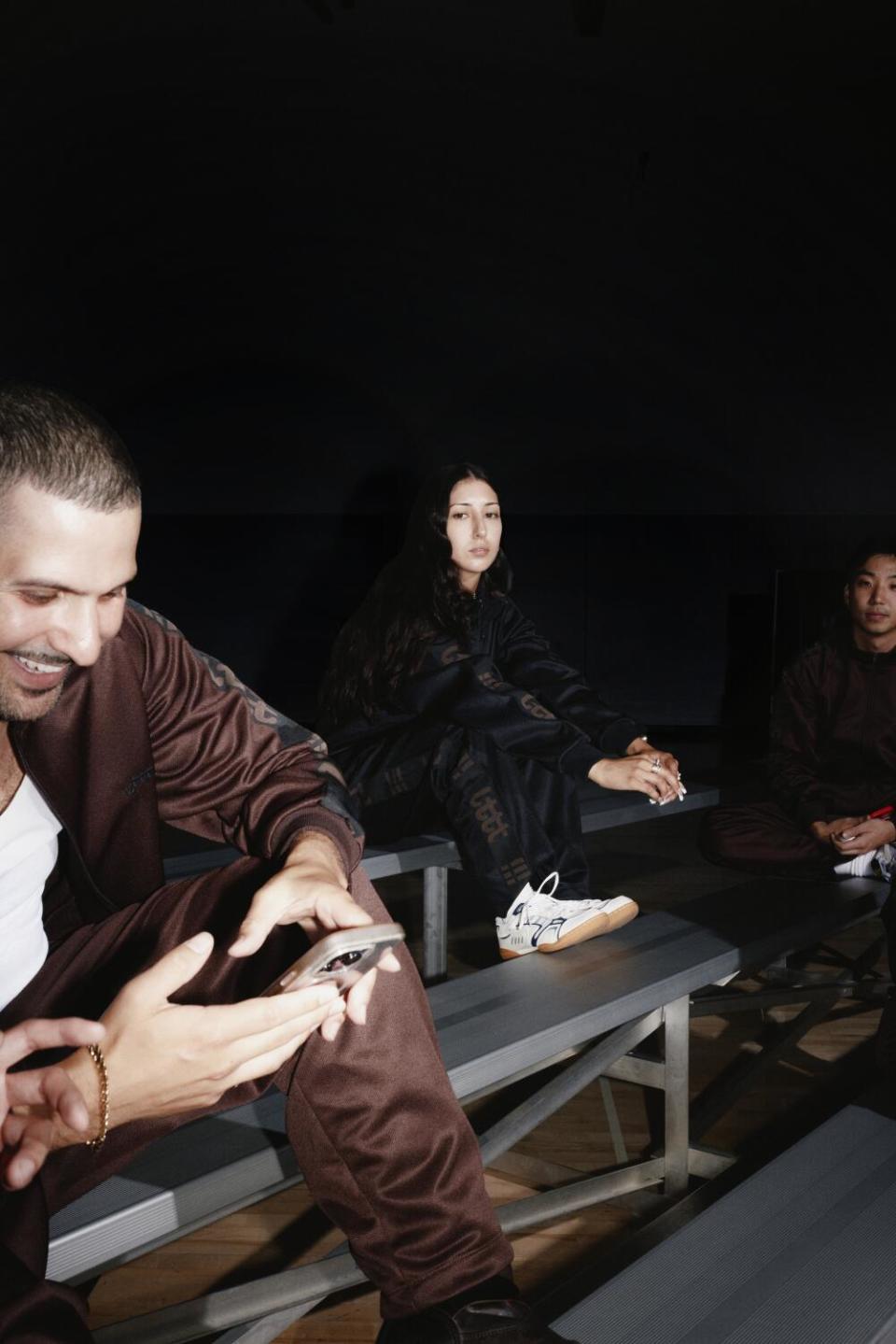 A photo of three people hanging out on bleachers in a dark gym.