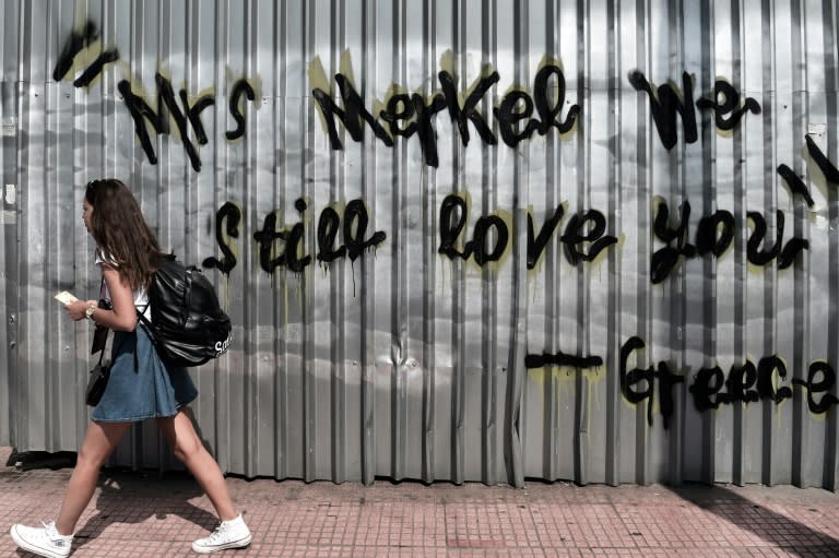 A young woman walks past graffiti reading 'Mrs Merkel we still love you - Greece' on display in Athens, on June 19, 2015