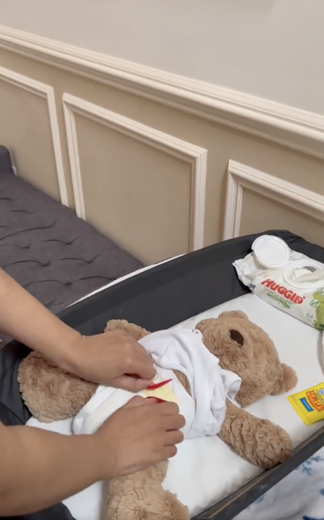 close up of Cardi's hands putting on a diaper on a teddy bear
