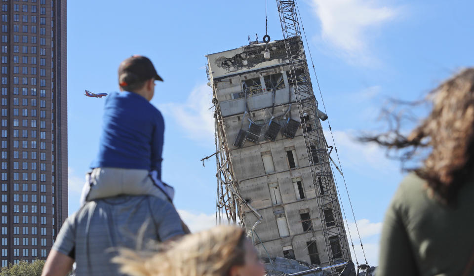 People gather to watch the demolition of the so called "Leaning Tower of Dallas" as a wrecking ball works to topple the structure north of downtown Dallas, Monday, Feb. 24, 2020. The still standing structure is part of an 11-story building that found a second life online after surviving a first demolition attempt. The former Affiliated Computer Services building inspired jokes and comparisons to Italy's Leaning Tower of Pisa when a Feb. 16 implosion failed to bring down its core. The company that engineered the blast said some explosives did not go off. (AP Photo/LM Otero)