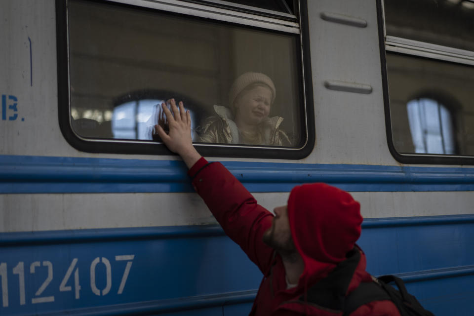 A child cries from inside a train while a man outside lifts his hand to the window.