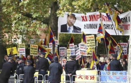 A police officer stands in front of pro-Tibet and Falun Gong protesters waiting for China's President Xi Jinping to pass on the Mall during his ceremonial welcome, in London, Britain, October 20, 2015. Xi is on a State visit to Britain. REUTERS/Neil Hall