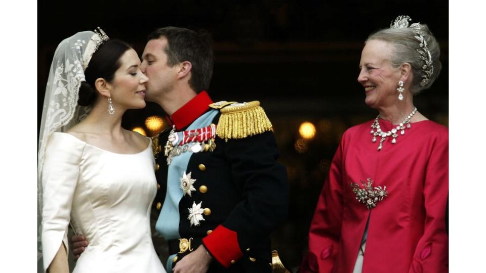 King Frederik kissing Queen Mary on the cheeck while Queen Margrethe looks on