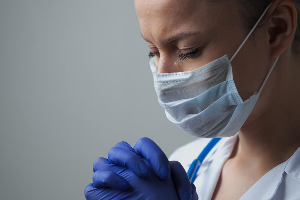 A female doctor therapist in a white robe, mask and gloves. Face close-up. The doctor cries and prays. Tears in eyes. Regret, anxiety and despair. Pandemic and virus epidemic. Coronavirus covid-19.