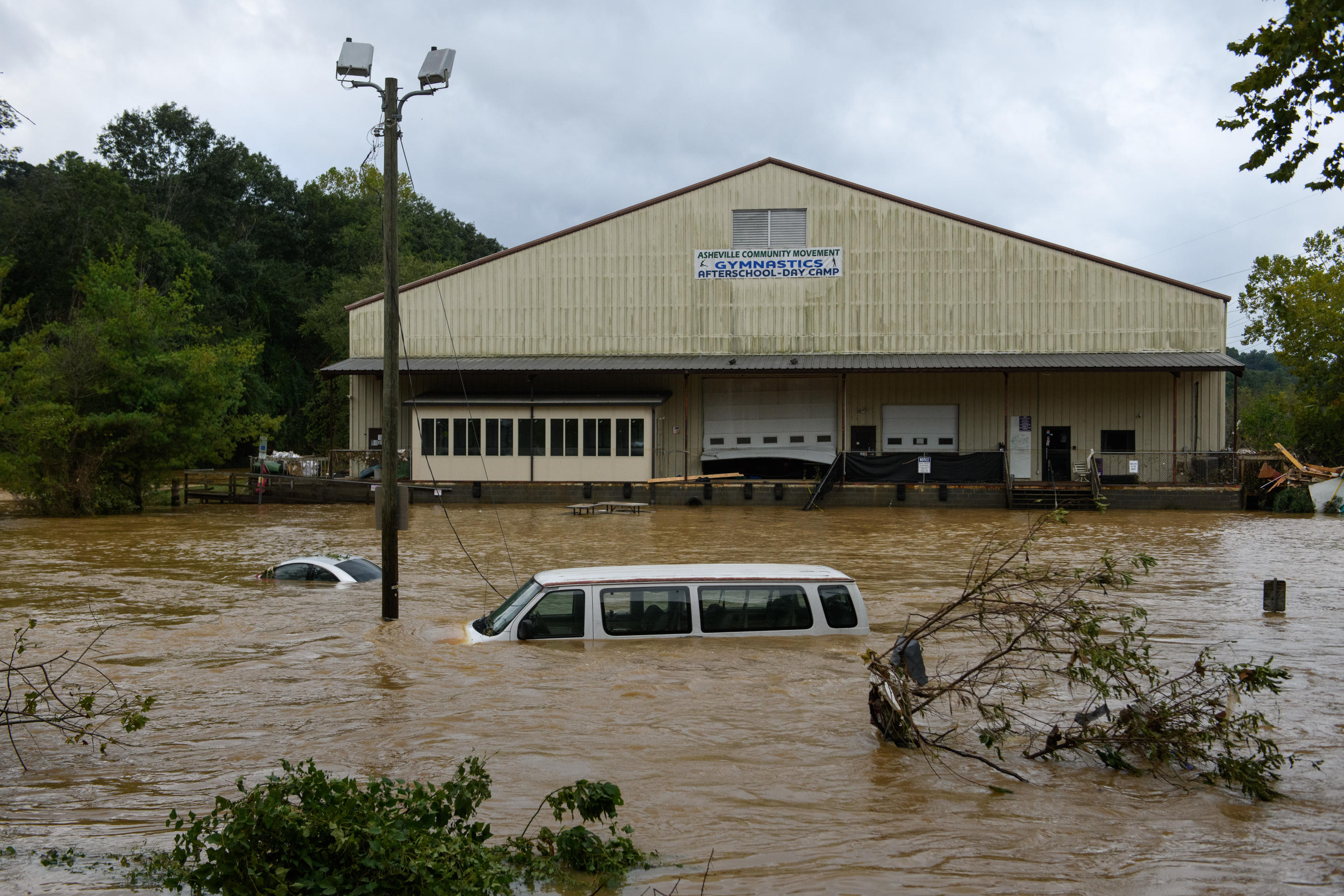 A car and a van in a flooded parking lot near a warehouse, with only the roofs of the vehicles visible.