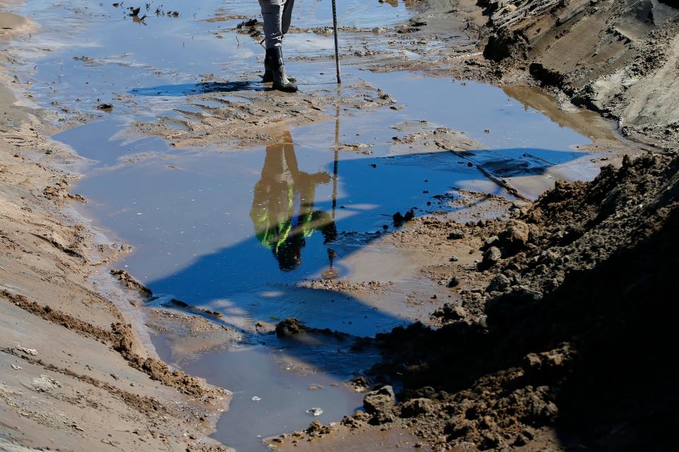 A surveyor reflects on the waters of the brook trench being dug during Phase 1 of the two-phase project by Buzzards Bay Coalition re-introducing marshes onto Marsh Island on the Fairhaven side of New Bedford's north harbor.