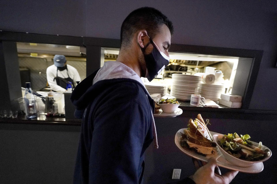 FILE - Bartender Denis Angelov carries plates of food from the kitchen, behind, at Tin Pan Alley restaurant, Tuesday, April 6, 2021, in Provincetown, Mass. The number of available jobs in the U.S. plummeted in August 2022 compared with July as businesses grow less desperate for workers, a trend that could cool chronically high inflation. (AP Photo/Steven Senne, File)