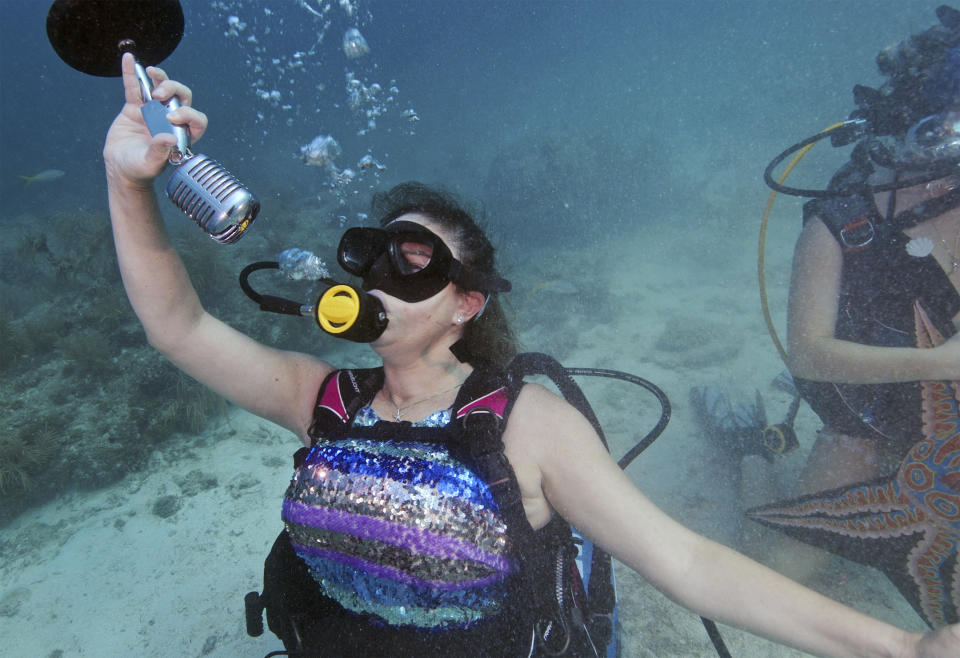 In this photo provided by the Florida Keys News Bureau, Kristen Livengood, left, pretends to sing underwater, Saturday, July 8, 2023, at the Lower Keys Underwater Music Festival in the Florida Keys National Marine Sanctuary near Big Pine Key, Fla. Several hundred divers and snorkelers submerged along a portion of the continental United States' only living coral barrier reef to listen to a local radio station's four-hour broadcast, piped beneath the sea to promote coral reef preservation. (Frazier Nivens/Florida Keys News Bureau via AP)