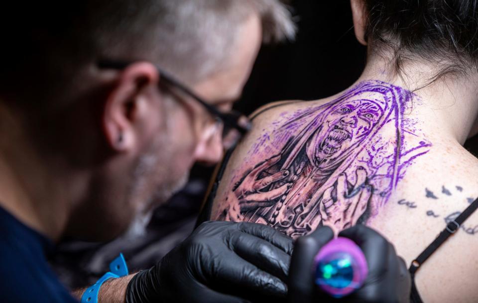 Jonathan Pinfield of Black Ball Tattoo draws up a tattoo on Christa Voss' back inside the GM Renaissance Center during the 27th annual Motor City Tattoo Expo in Detroit on Saturday, March. 4, 2023.