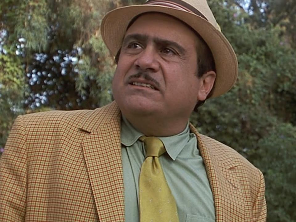 Danny DeVito as Harry Wormwood in a yellow suit, green shirt, a yellow tie, and a yellow fedora