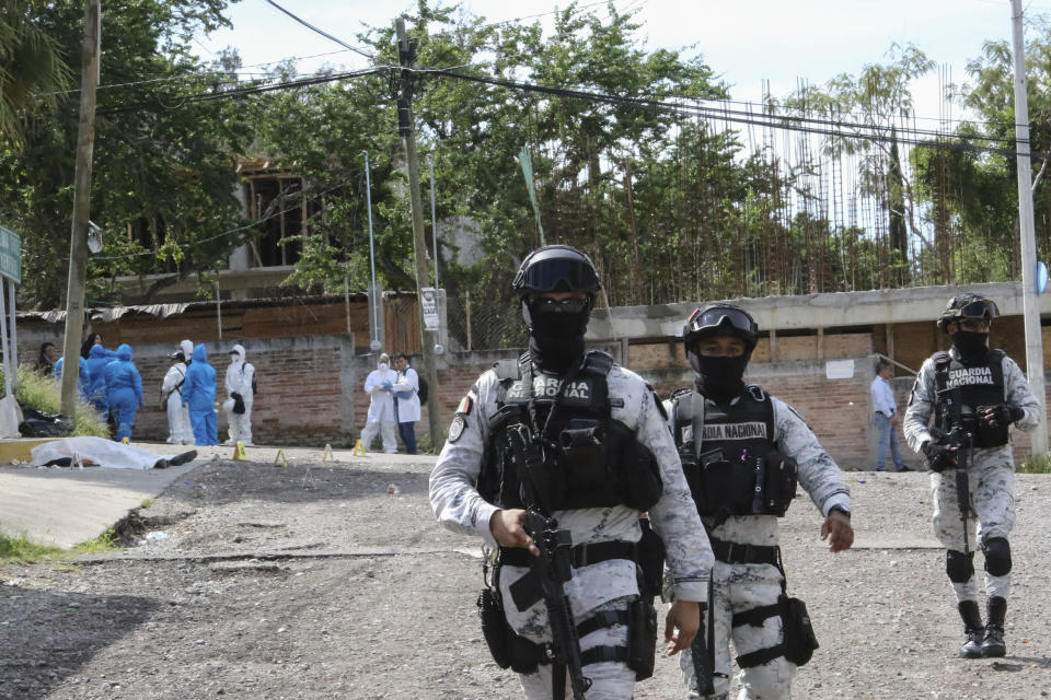 The body of Fernando García Fernández, the representative of Mexico’s Attorney General’s office in the southern state of Guerrero, lies covered by a white cloth, background on left, as National Guardsmen patrol the area, in Chilpancingo, Mexico, Tuesday, Sept. 12, 2023. Gunmen killed García Fernández on Tuesday, according to authorities. (AP Photo/Alejandrino Gonzalez)