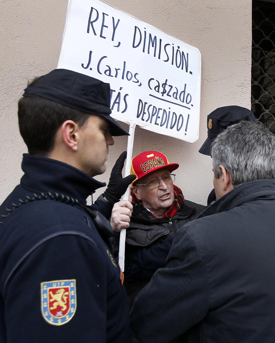 Police men talk to a protestor, centre, who shows a banner reading "King, resign! Juan Carlos, hunted, you are fired" as Spain's King Juan Carlos leaves from San Jose hospital where he received medical treatment in Madrid, Spain, Wednesday, April 18, 2012. Spain's King Juan Carlos says he is sorry for having gone on African elephant-hunting trip. In an unprecedented gesture, the 74-year-old monarch said he was "very sorry. I made a mistake. It won't happen again." The king came under scathing criticism this week after he went on a safari trip to Botswana as Spain writhes in its one of its worst ever economic crises. The trip came to light when the king ended up having to be taken to hospital for hip treatment after having fallen. (AP Photo/Andres Kudacki)