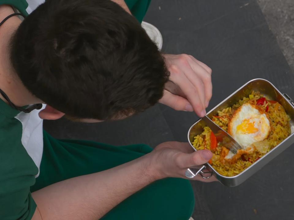 Overhead shot of man eating rice with a fried egg in it.