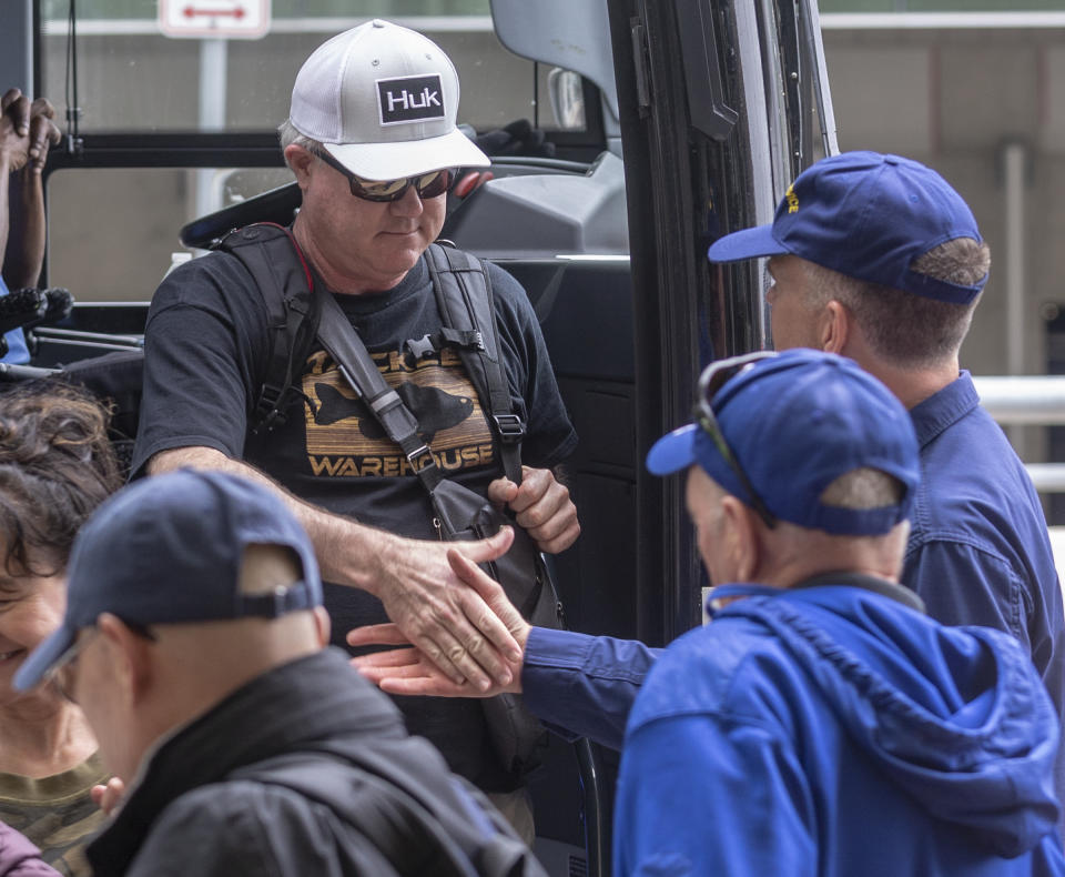 A man in a white hat shakes hands with people at San Antonio International Airport Tuesday, March 3, 2020 as he gets off a bus that arrived from JBSA-Lackland. People evacuated from the coronavirus-infected Diamond Princess cruise ship in Japan had been held in quarantine at Lackland to ensure they were not infected with the virus. (William Luther/The San Antonio Express-News via AP)