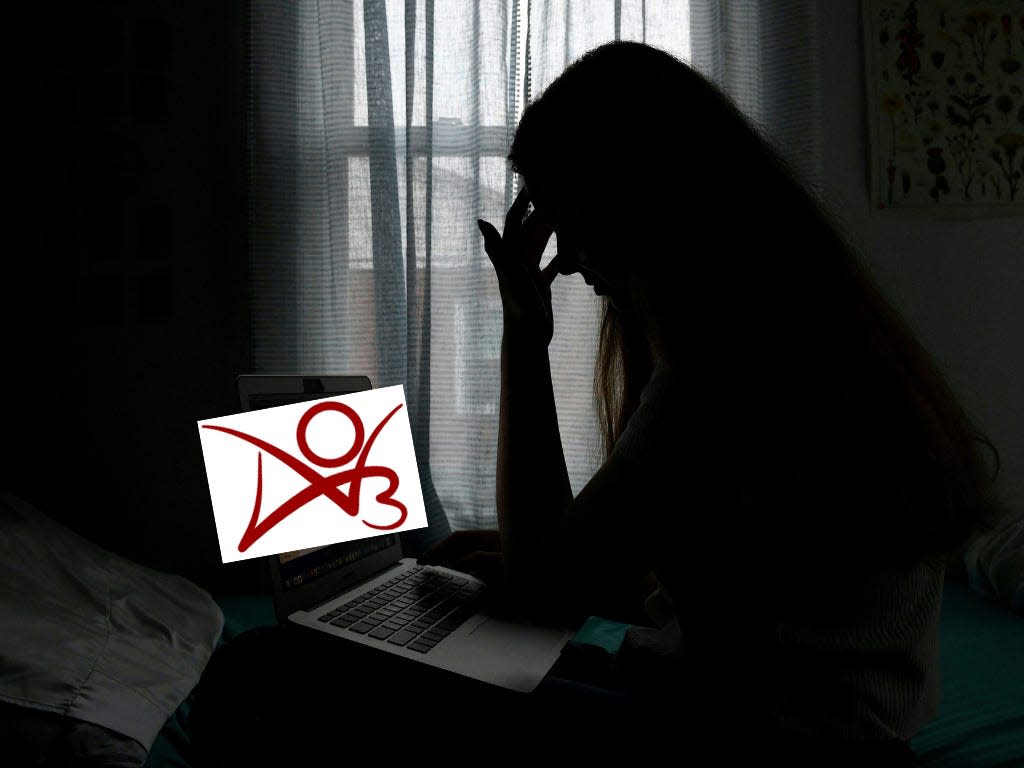 A woman silhoutted in darkness, looking at a laptop. The laptop's screen has been replaced with the composite image of the AO3 logo.