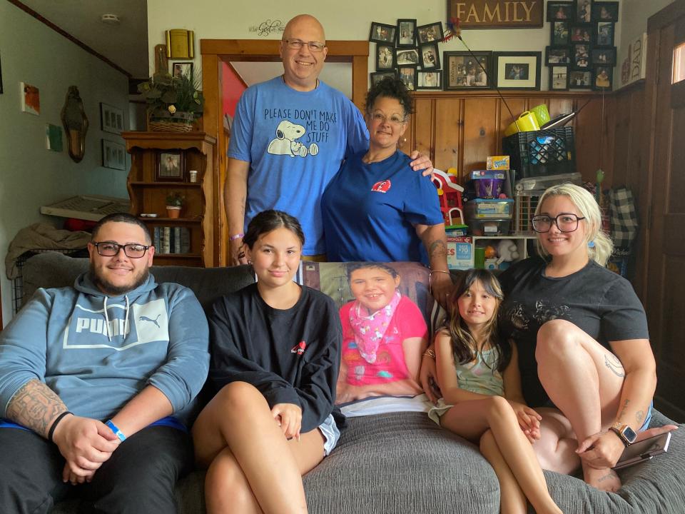 Emily Santarpia's family surrounds a blanket with her photo on it in their Taunton home on Monday, July 10, 2023. Front row, from left, Michael Moniz (brother); Kimberly Santarpia (twin sister); Audriana Cavaco (niece); and Melissa Cavaco (sister); back row, from left, Emily's parents John Santarpia and Maria Santarpia. Emily died in January at the age of 13 from complications from a rare genetic condition called isodicentric 15.