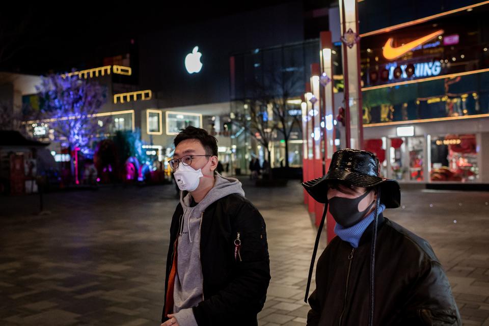 People wearing a protective facemask to protect against the COVID-19 coronavirus walk past an Apple store (top L) and a Nike shop (top R) outside of a nearly empty shopping mall, minutes after rush hour, in Beijing on February 24, 2020. - The novel coronavirus has spread to more than 25 countries since it emerged in December and is causing mounting alarm due to new outbreaks in Europe, the Middle East and Asia. (Photo by NICOLAS ASFOURI / AFP) (Photo by NICOLAS ASFOURI/AFP via Getty Images)