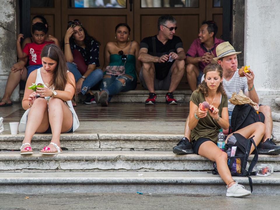A group of tourists eat their lunch on the steps of the "Procuratie" in Venice