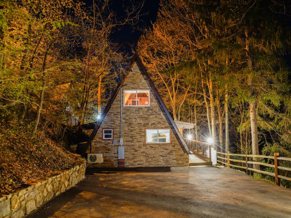 exterior shot of A-frame cabin at night, Joey Hadden, " I spent 2 nights in a cozy A-frame cabin for the first time while visiting the Great Smoky Mountains"