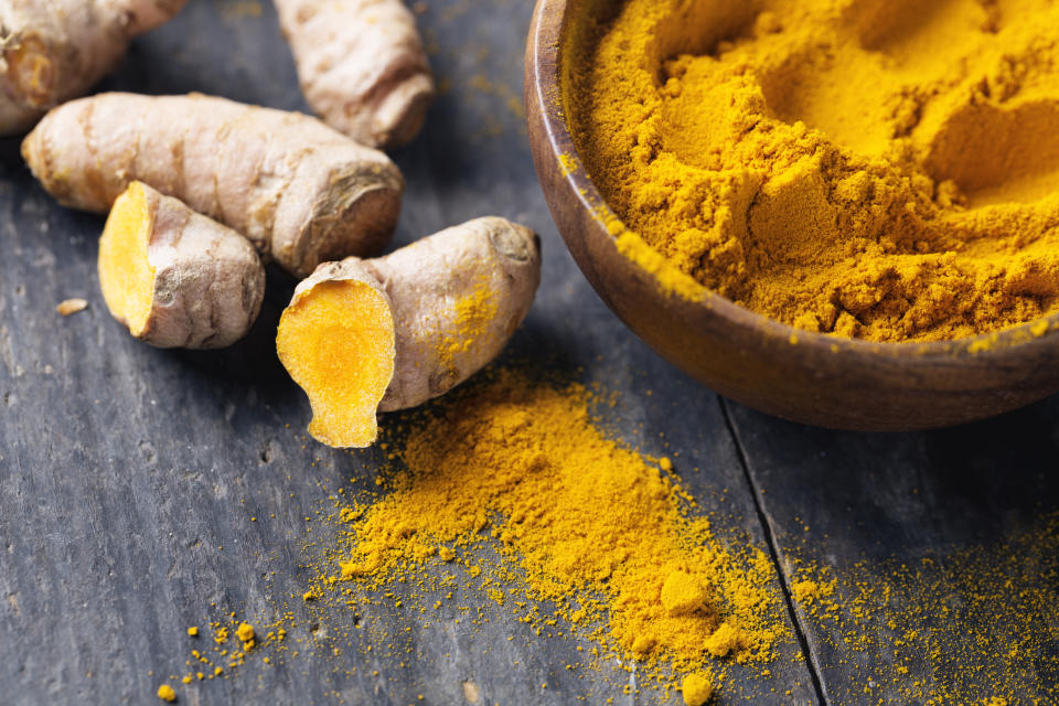 Freh turmeric roots and turmeric powder in a wooden bowl on rustic wood