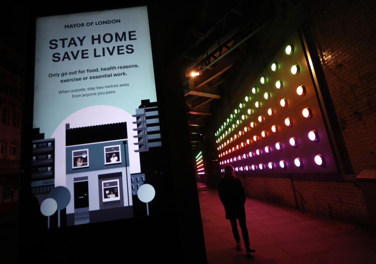 A woman walks between a coronavirus information sign and a light installation near London Bridge, London, as the UK continues in lockdown to help curb the spread of the coronavirus.
