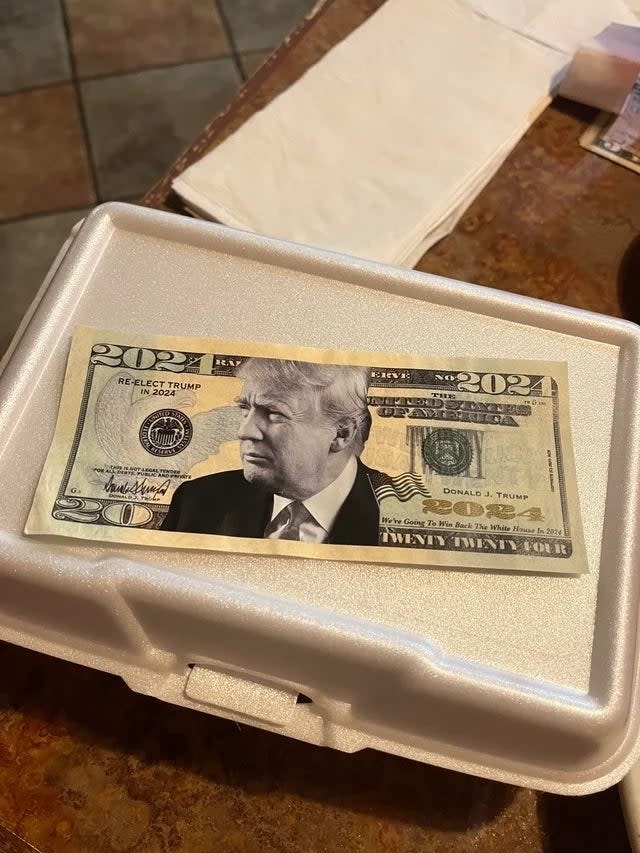 A fake twenty-dollar bill with former President Donald Trump's face superimposed is placed on a styrofoam container