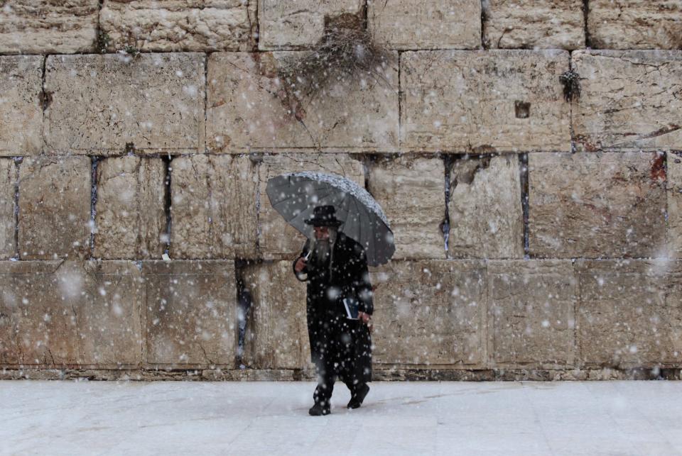 A man holding an umbrella walks as snow falls at the Western Wall in winter in Jerusalem's Old City