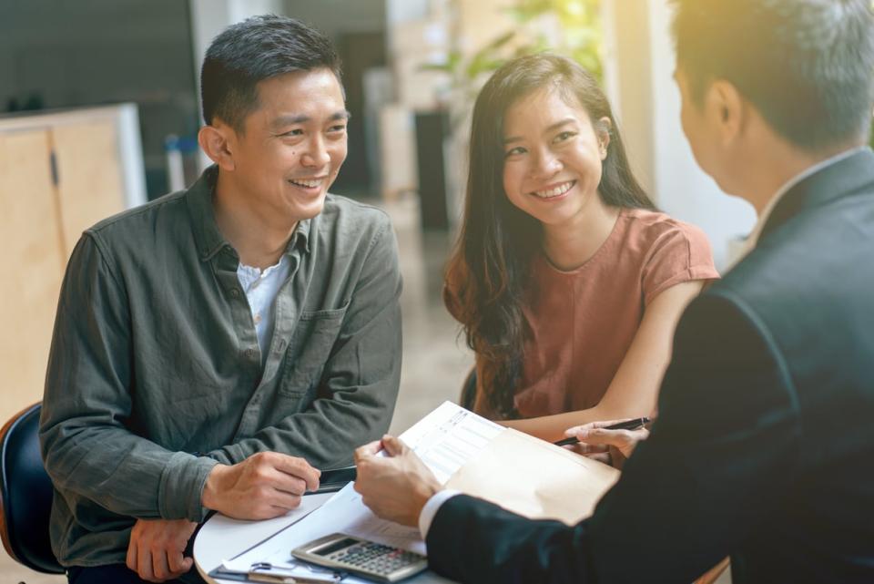 Two people smile while going over documents with another person. 