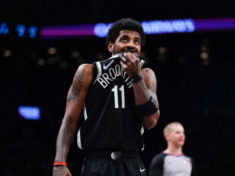 Kyrie Irving looks up and holds his jersey over his mouth during a Nets game in 2022.