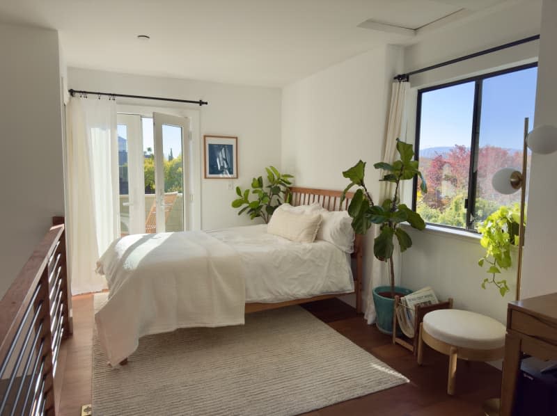 Slated wood headboard, white linens, beige rug, wood and metal loft railing, house plants, balcony doors